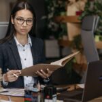 Confident businesswoman in professional attire reviewing documents at her desk in a modern office setting.